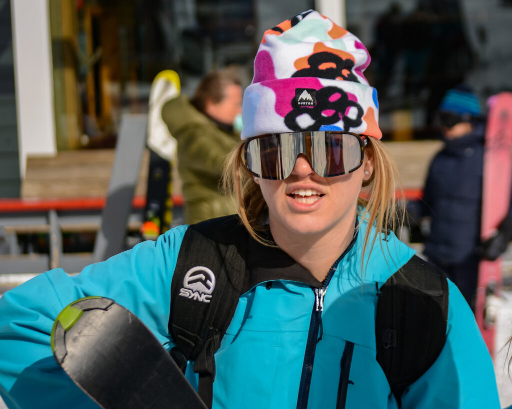 Hazel Harris, in white ski cap and goggles, blue-green parka.